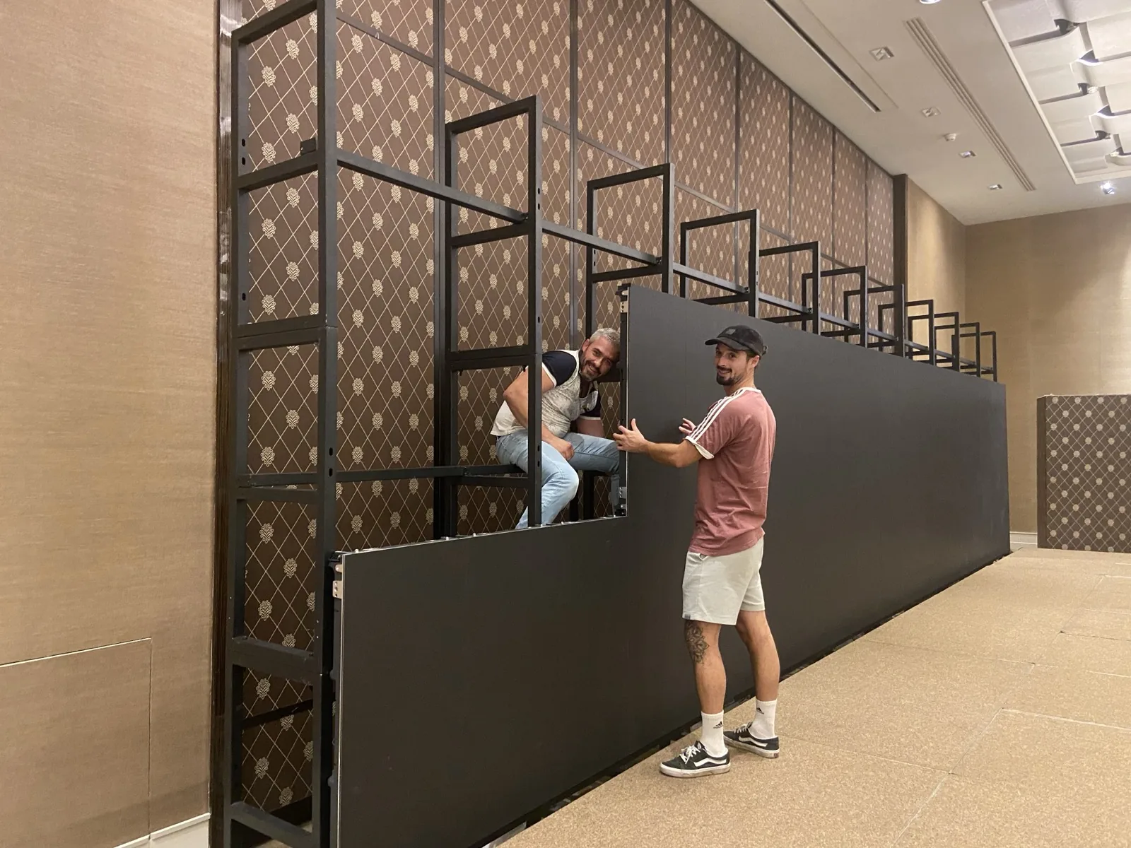 Zwei Techniker von HYPERVISUAL montieren während einer Installation ein LED-Panel auf dessen Rahmen