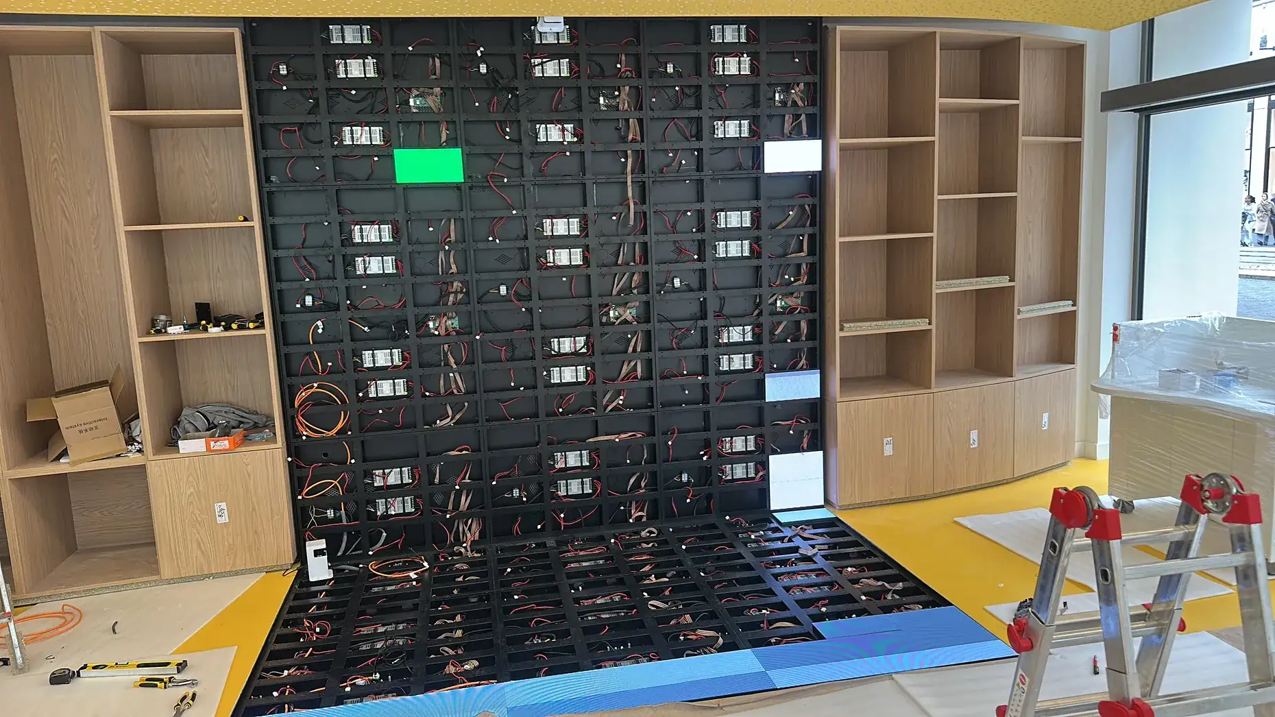 Front of an indoor LED wall during assembly between two wooden bookcases, cabling visible