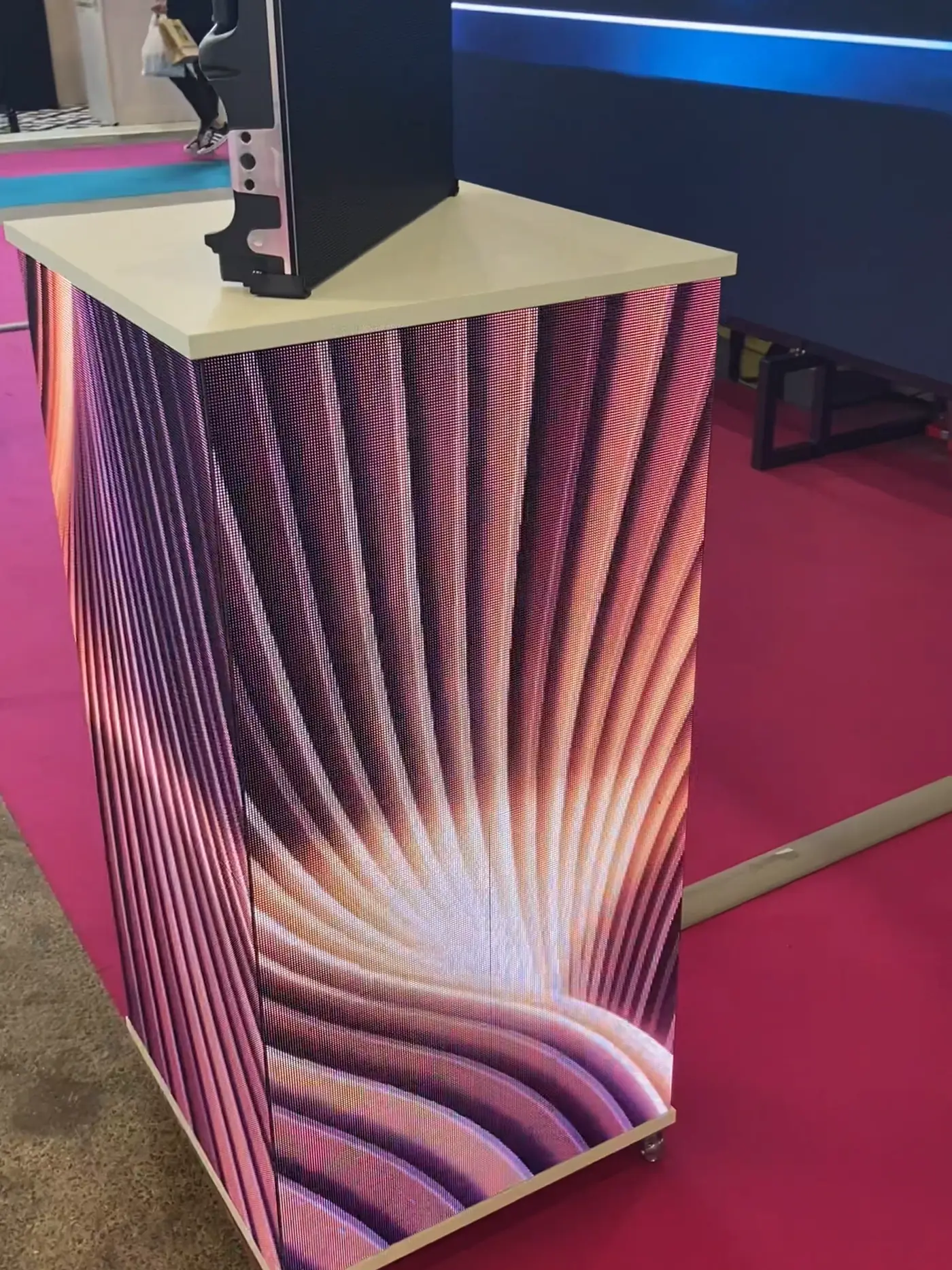 LED high table at a trade show, a fan of peach and violet light running round the corner between two of its faces