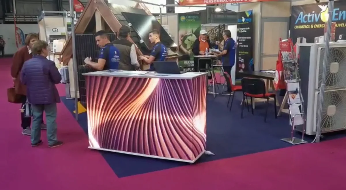 Comptoir d’accueil LED aux faces ornées d’un motif de vagues roses, sur un stand de salon