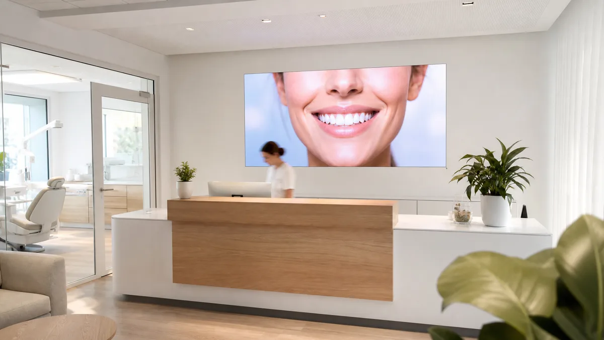 Bright clinic reception, an LED screen above the desk showing a smile, a receptionist at work