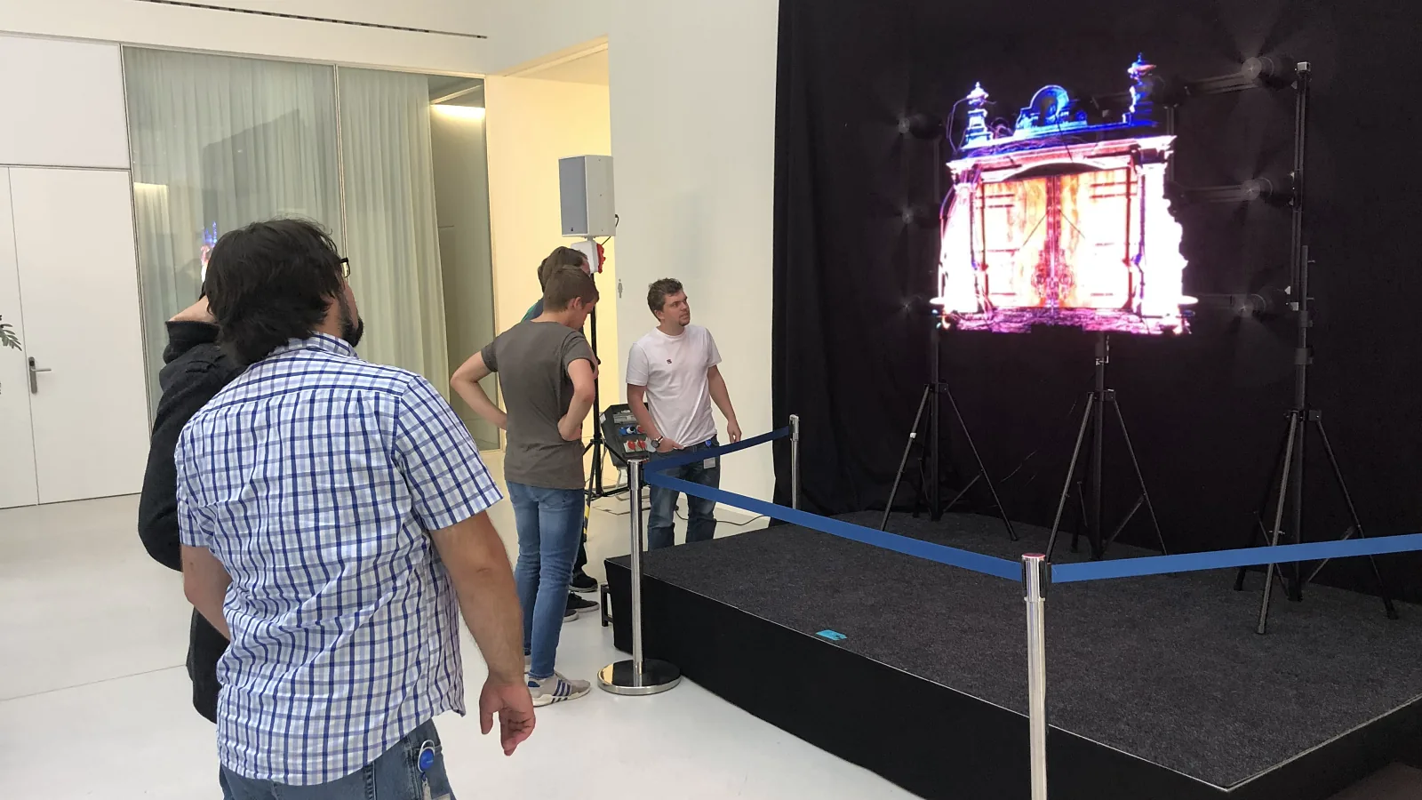 HYPERVSN hologram floating above a small stage with a black backdrop, a visitor watching
