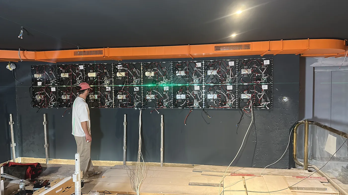 A technician in a shop checking a row of LED cabinets fixed to the back wall along a green laser line