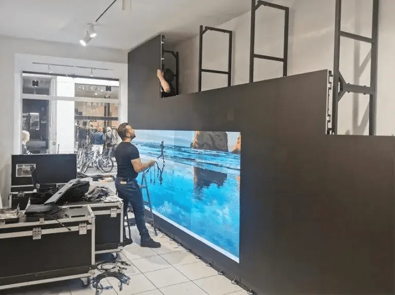 A technician fitting the panels of a large LED screen in a showroom, flight cases on the floor