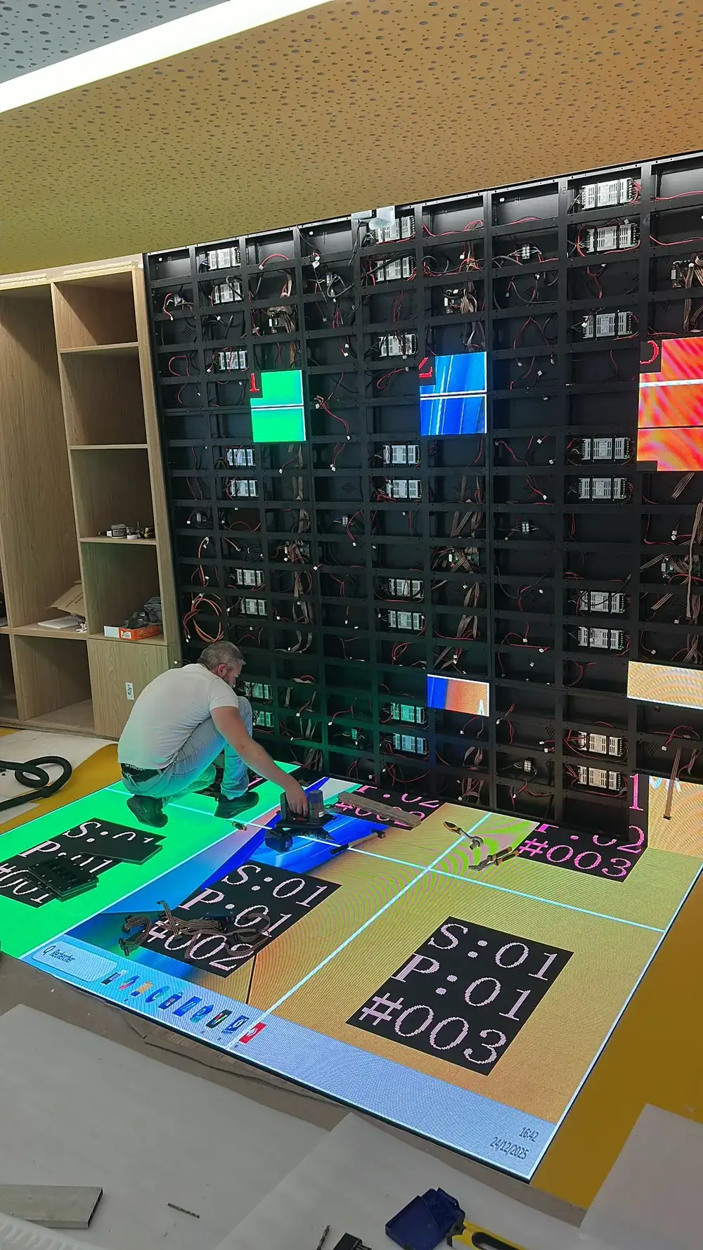 LED screen under construction below a yellow ceiling, modules lit in green, blue and red while the panels are addressed