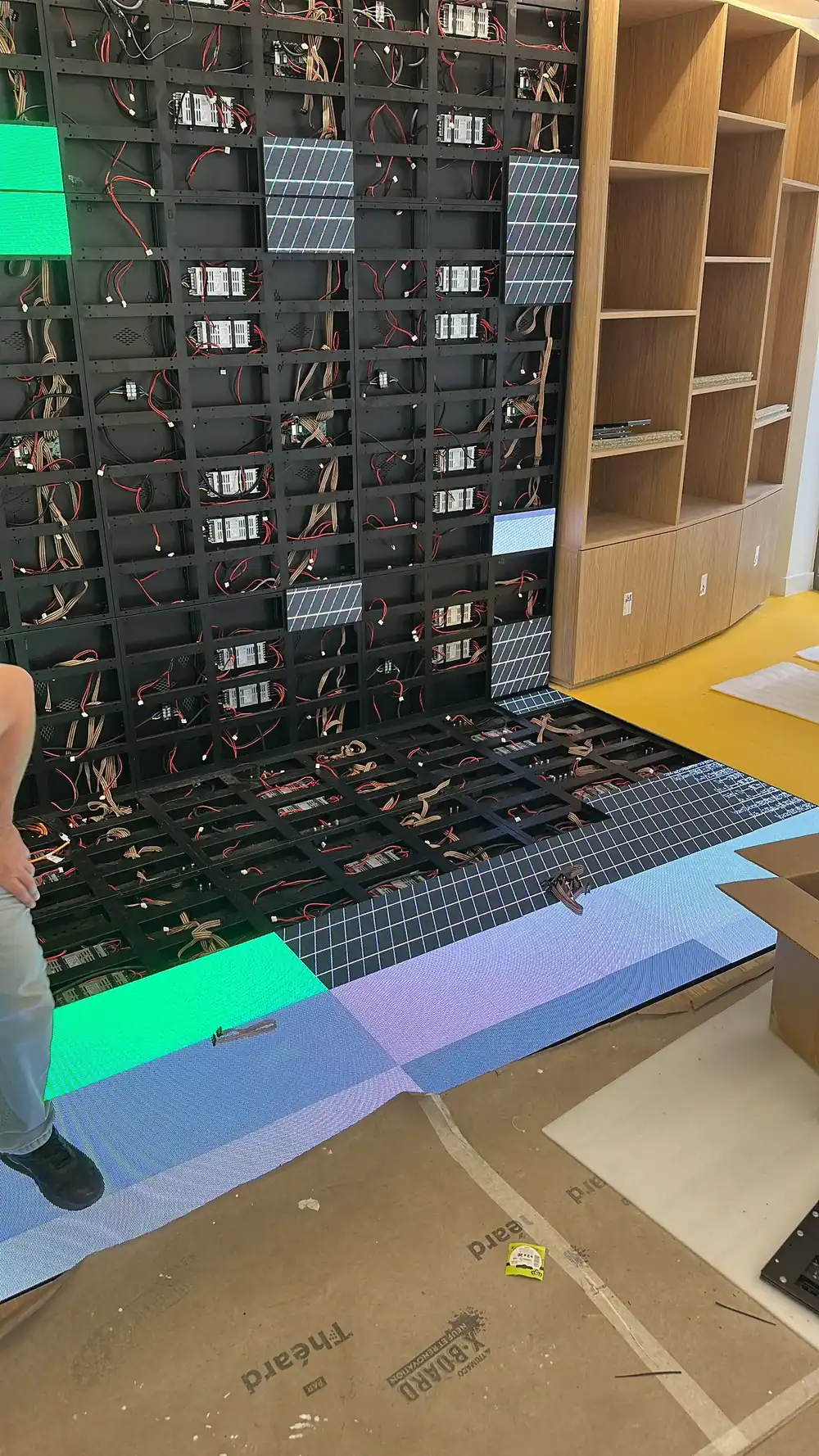Close view of an LED screen frame during assembly: cards and cables on each panel, a few modules already fitted, oak shelves on the right