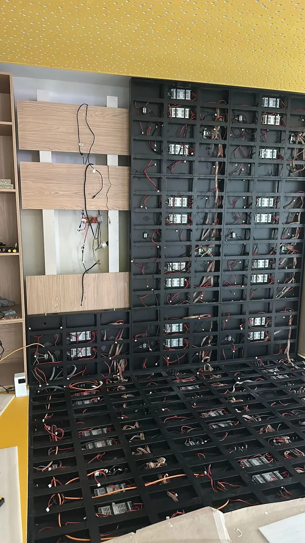 LED screen frame fixed to a shop wall under a yellow ceiling, cables coming out of the wall beside oak panels