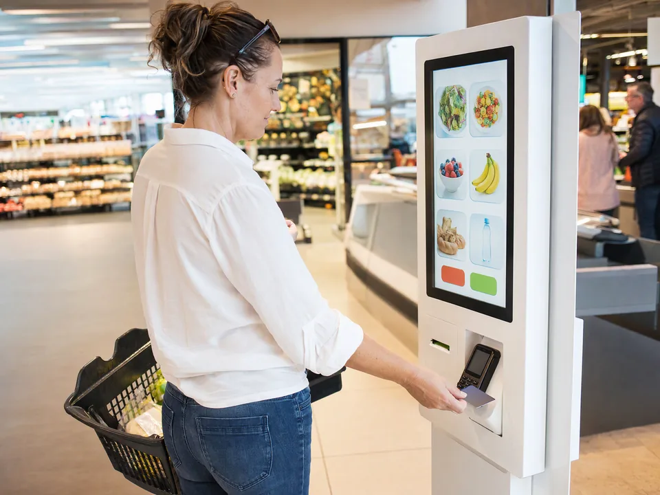 Shopper with a basket paying by card at a self-service kiosk in a grocery store