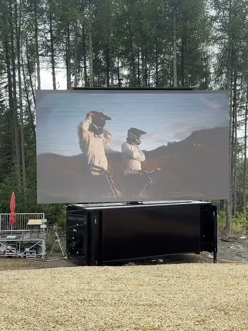 LED trailer screen raised in a forest clearing, two mountain bikers on screen