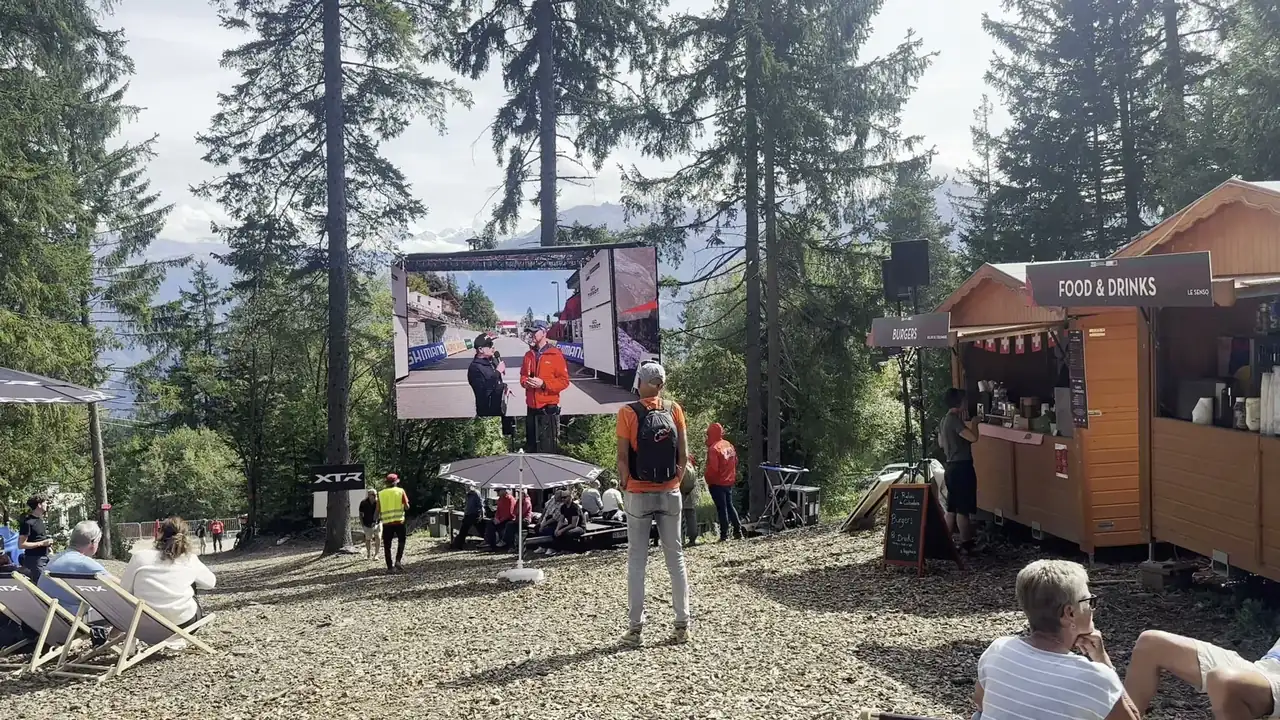 LED trailer screen above deckchairs and a food stand at an outdoor sports event in a forest clearing