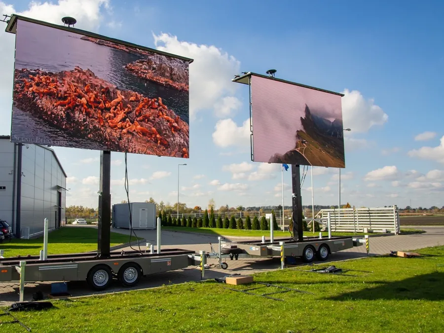 Two LED trailers with their screens raised on masts in a field, each showing a picture