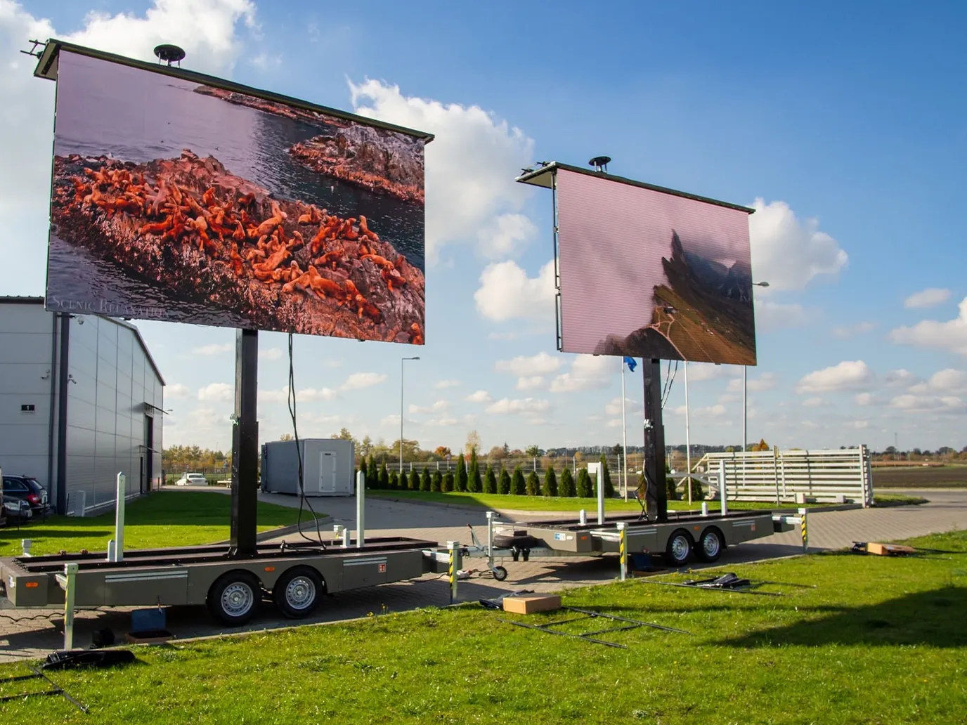 Two LED trailers side by side on grass, their screens raised