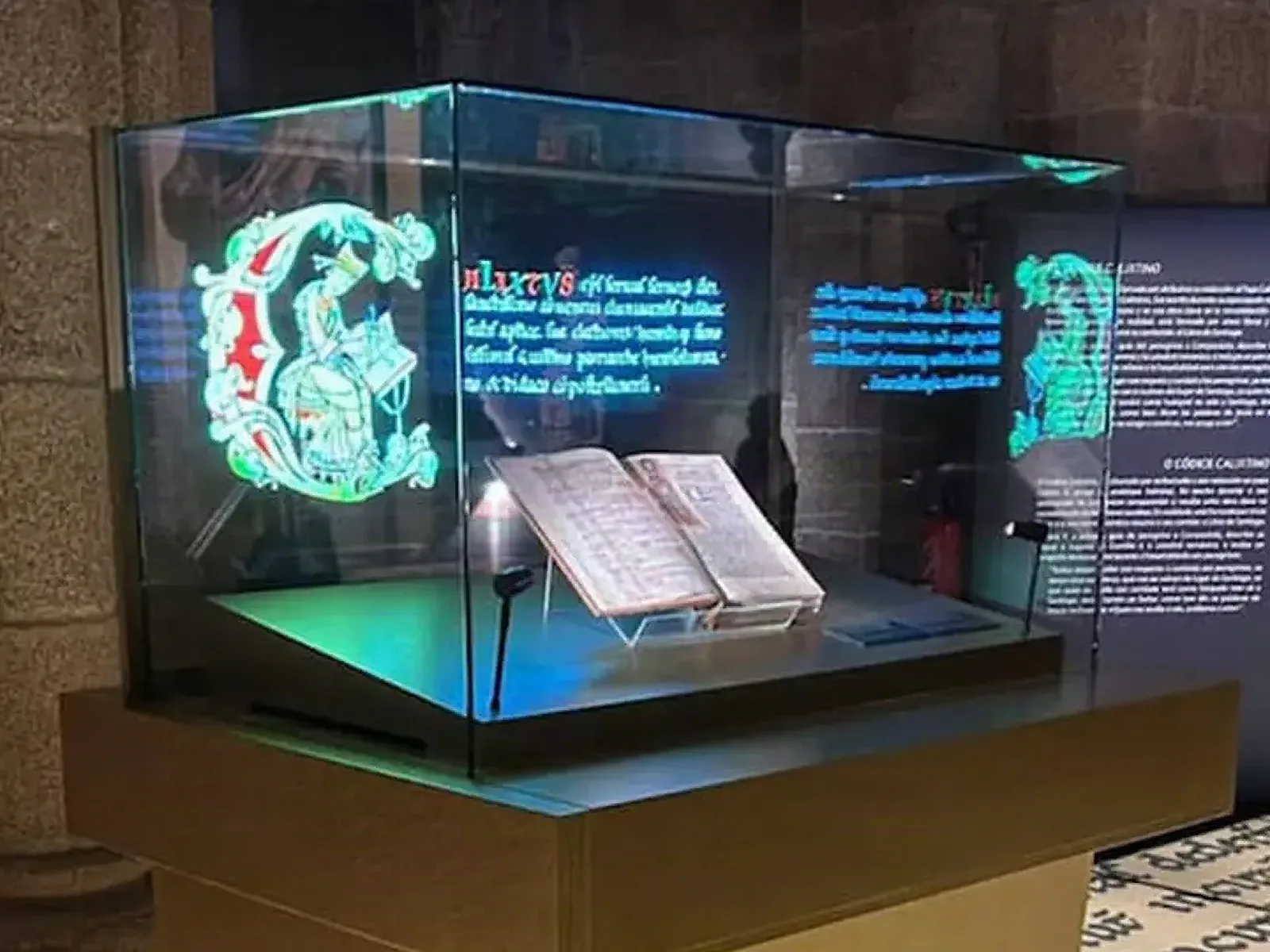 Museum display case where glowing illuminated letters play on the glass around an open manuscript