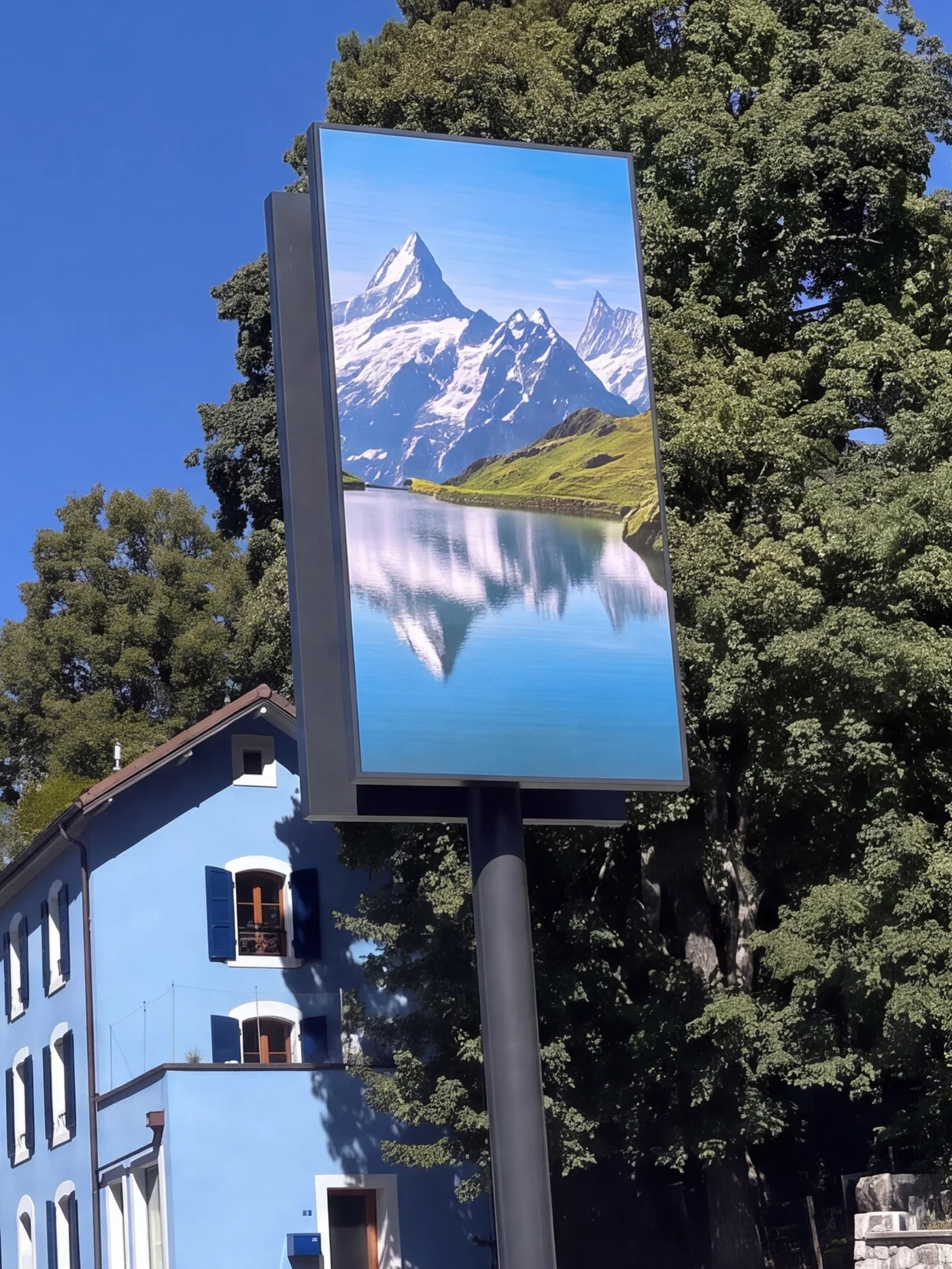 Outdoor LED screen on a mast in front of a building, the picture a mountain landscape under a clear sky