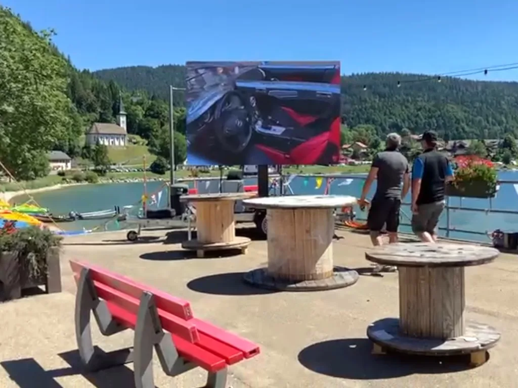 Outdoor LED screen on a trailer beside a lake during a public event