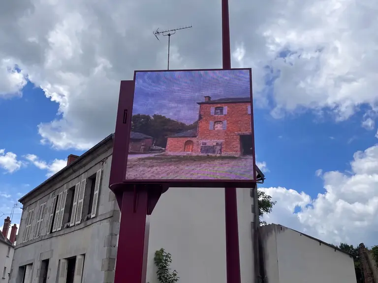 Outdoor LED screen on a mast in front of a building, seen from the street