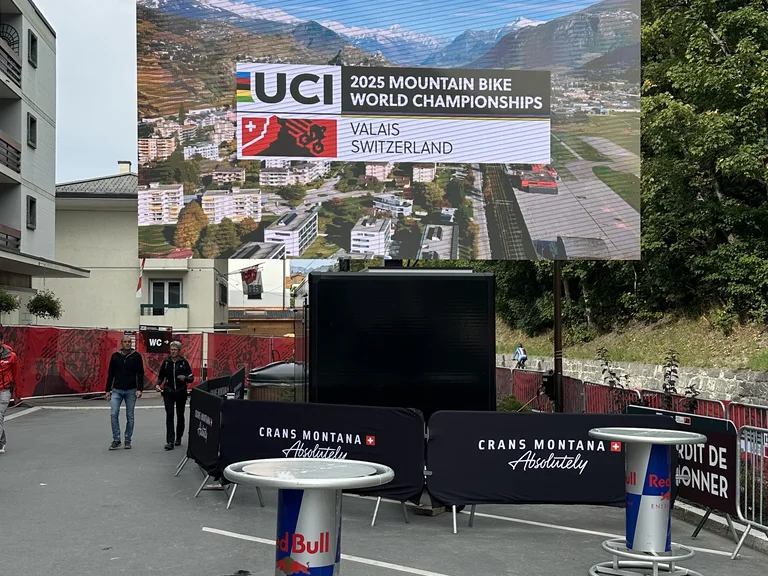 Outdoor LED screen on a trailer at a mountain-bike event, with the finish area behind