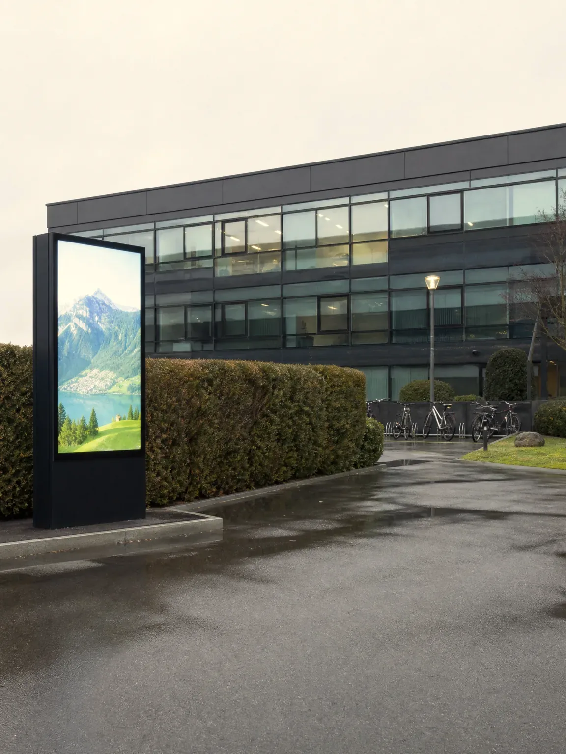 Outdoor digital totem in front of an office building, a mountain landscape on screen