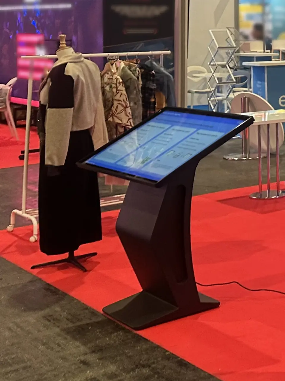 Touchscreen kiosk on a K-shaped column, its screen tilted towards the user, on a trade-show stand