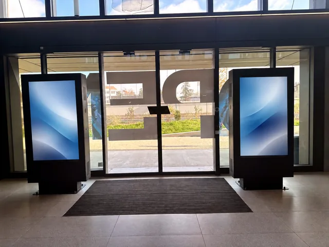 Two digital totems standing either side of a glass entrance door, a doormat between them