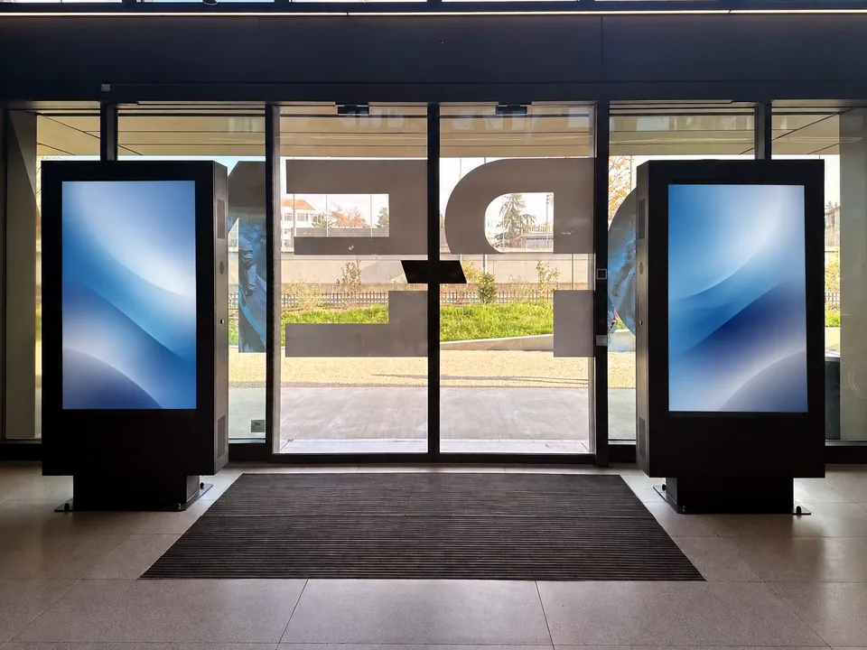 Zwei digitale Totems, die den Glaseingang einer Firmenlobby einrahmen