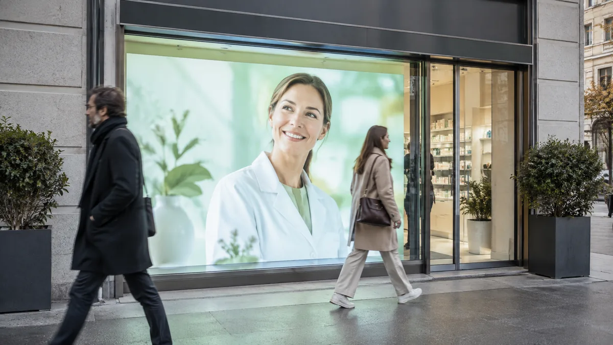 LED wall filling the window of a pharmacy in daylight, two people walking past
